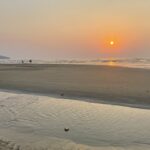 The sun setting through a hazy sky over a sandy beach in Goa, India.